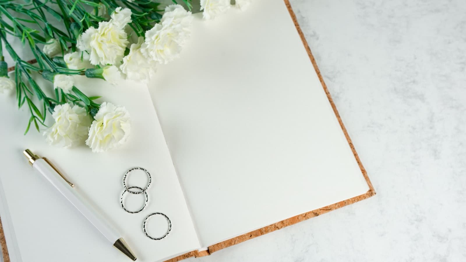 Open blank notebook with a pen and two rings beside white carnations